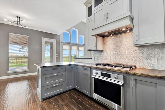 kitchen featuring crown molding, backsplash, appliances with stainless steel finishes, dark hardwood / wood-style floors, and kitchen peninsula