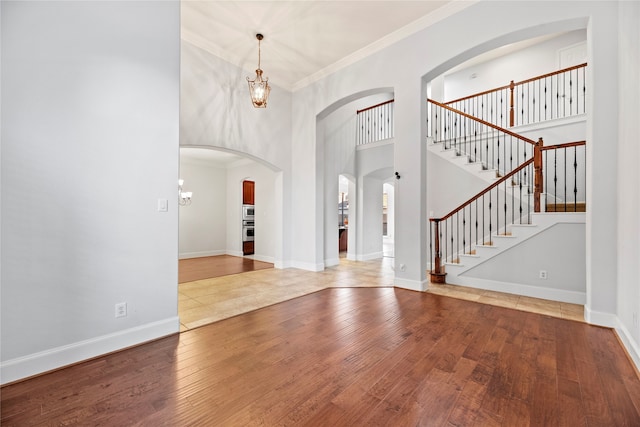 foyer featuring a chandelier, wood-type flooring, a towering ceiling, and crown molding