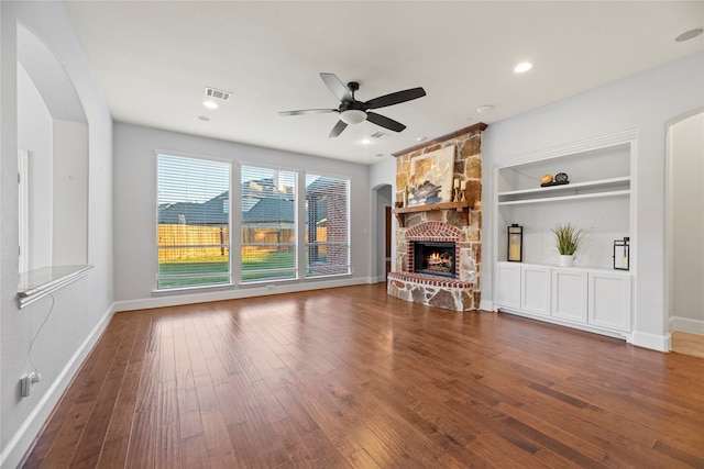 unfurnished living room featuring built in shelves, a stone fireplace, dark hardwood / wood-style flooring, and ceiling fan