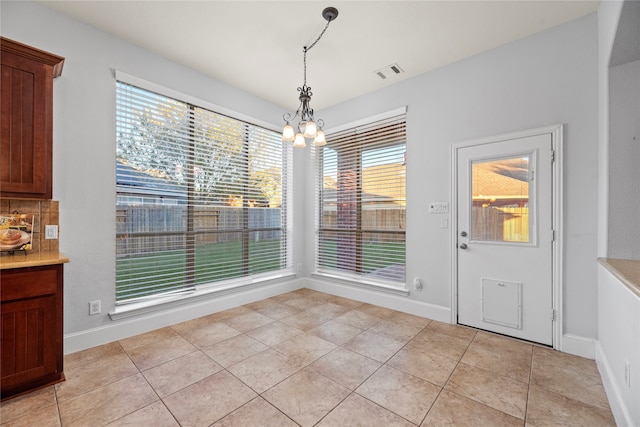 unfurnished dining area with a notable chandelier, a healthy amount of sunlight, and light tile patterned flooring