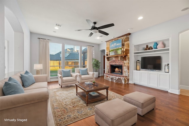 living room featuring hardwood / wood-style floors, ceiling fan, built in features, and a fireplace