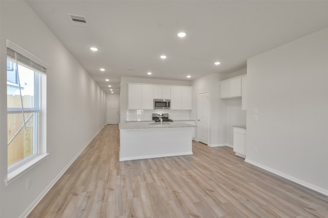 kitchen with white cabinets, light stone counters, light hardwood / wood-style floors, and stainless steel appliances