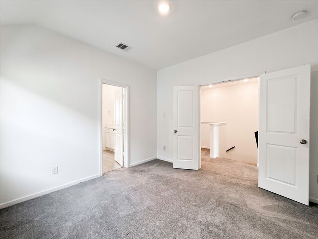 unfurnished bedroom with connected bathroom, carpet flooring, and vaulted ceiling