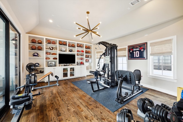 exercise room featuring a notable chandelier, vaulted ceiling, and hardwood / wood-style flooring