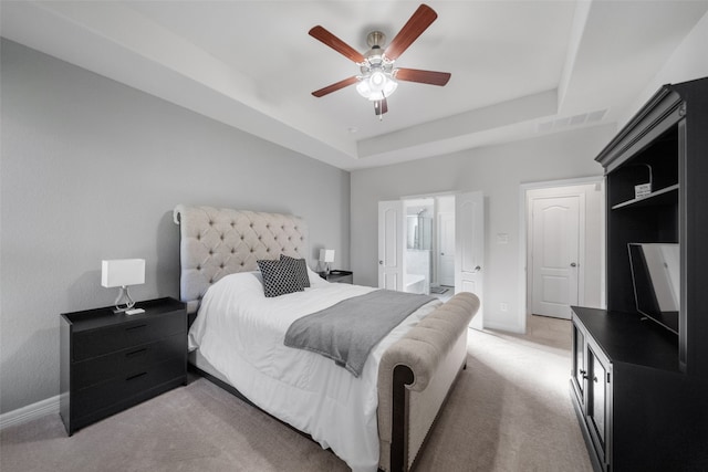 bedroom with connected bathroom, a tray ceiling, light carpet, and ceiling fan