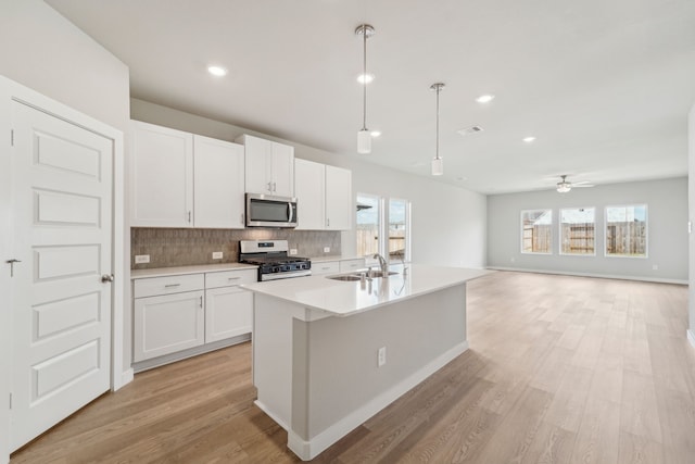 kitchen featuring tasteful backsplash, hanging light fixtures, white cabinets, stainless steel appliances, and a center island with sink