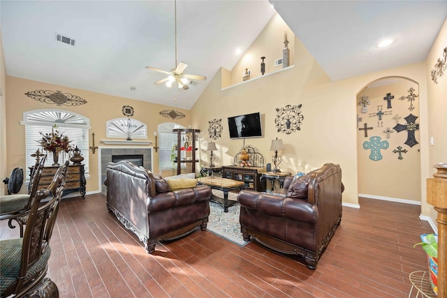 living room featuring dark hardwood / wood-style flooring, a tiled fireplace, high vaulted ceiling, and ceiling fan