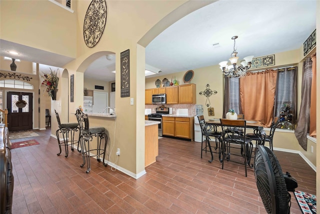 kitchen with stainless steel appliances, decorative light fixtures, a kitchen bar, an inviting chandelier, and hardwood / wood-style flooring