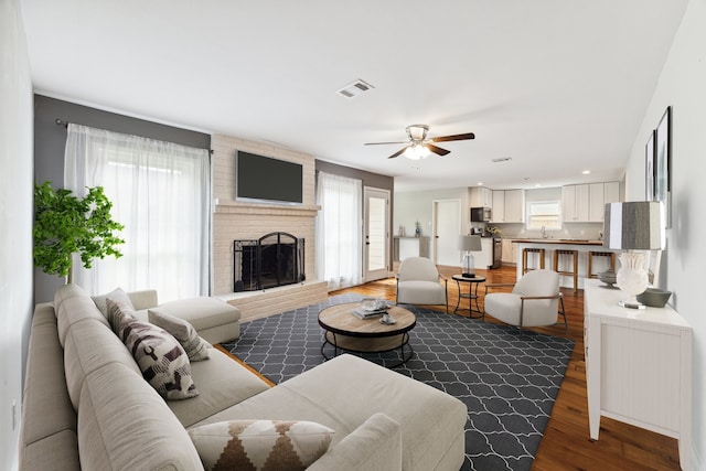 living room with a fireplace, hardwood / wood-style flooring, ceiling fan, and sink