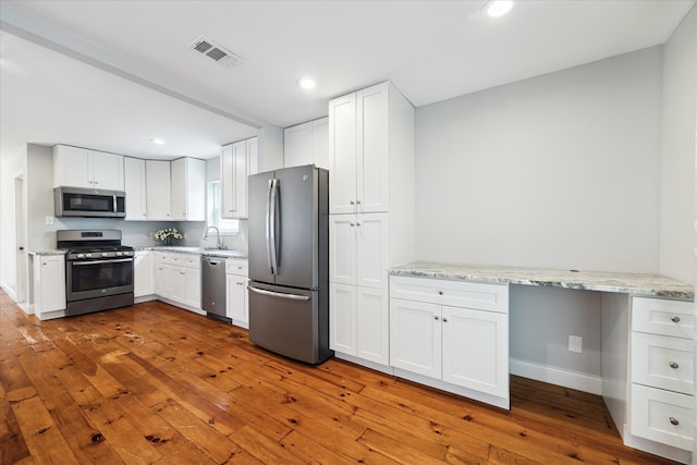 kitchen with light hardwood / wood-style floors, white cabinets, sink, light stone countertops, and appliances with stainless steel finishes