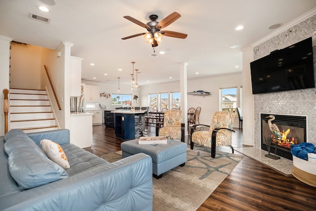 living room featuring ceiling fan, dark hardwood / wood-style flooring, ornamental molding, and a tiled fireplace