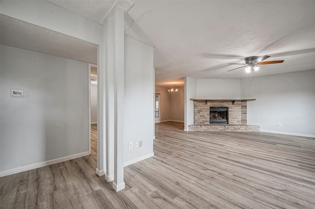 unfurnished living room featuring a fireplace, ceiling fan with notable chandelier, a textured ceiling, and light hardwood / wood-style flooring