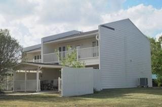 rear view of property featuring a lawn, a balcony, and central AC unit