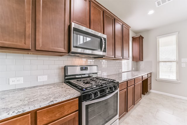 kitchen featuring stainless steel appliances, light tile patterned floors, backsplash, and light stone countertops