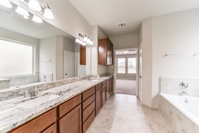 bathroom with a relaxing tiled tub, vanity, and tile patterned floors