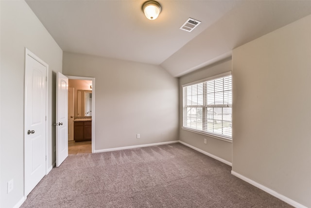 unfurnished bedroom featuring connected bathroom, vaulted ceiling, and light colored carpet