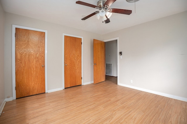 unfurnished bedroom with light wood-type flooring, multiple closets, and ceiling fan