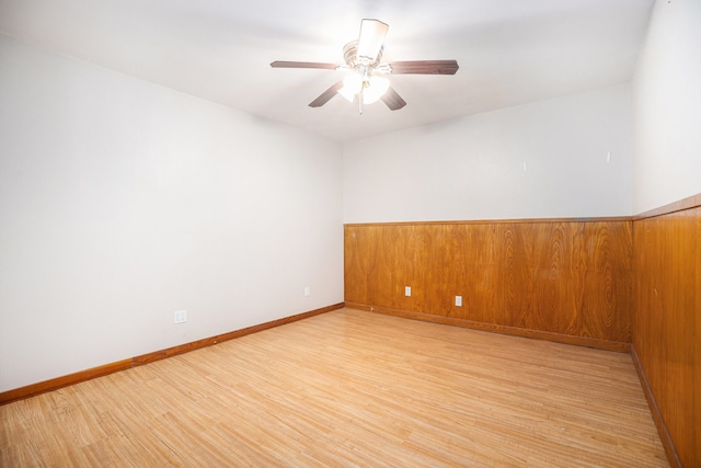 spare room featuring light hardwood / wood-style flooring, wooden walls, and ceiling fan