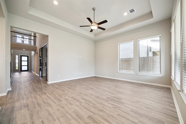 spare room with ceiling fan, a healthy amount of sunlight, light hardwood / wood-style flooring, and a tray ceiling