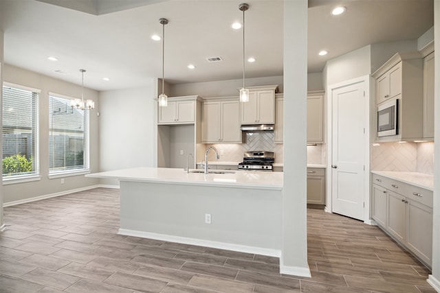 kitchen featuring stainless steel appliances, hanging light fixtures, sink, an island with sink, and light wood-type flooring