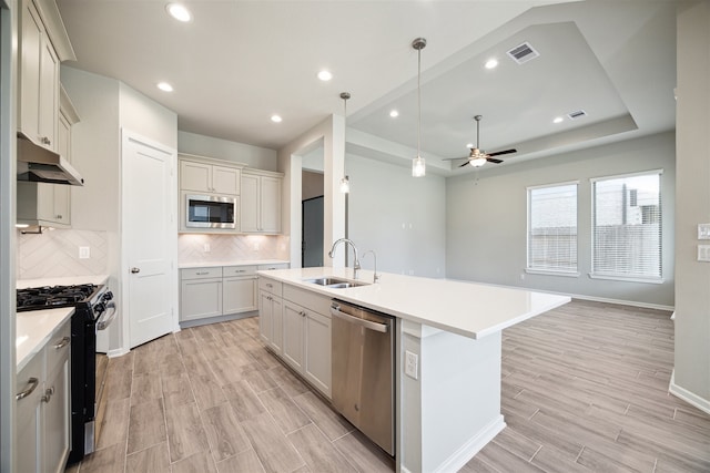 kitchen with stainless steel appliances, sink, an island with sink, backsplash, and light hardwood / wood-style flooring