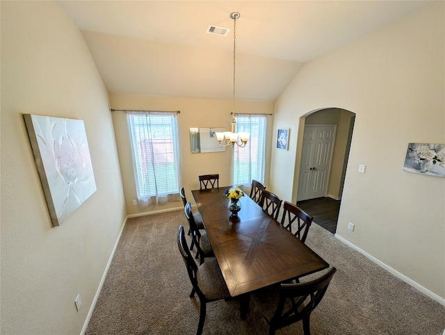 carpeted dining room featuring an inviting chandelier and vaulted ceiling