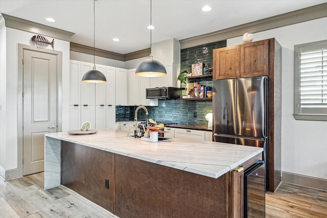 kitchen with light wood-type flooring, decorative light fixtures, light stone countertops, beverage cooler, and a kitchen island with sink