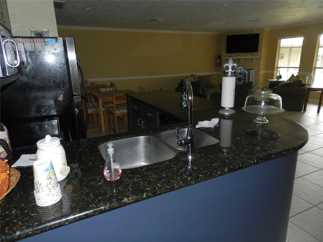 kitchen with sink, ornamental molding, dark stone counters, light tile patterned floors, and black refrigerator