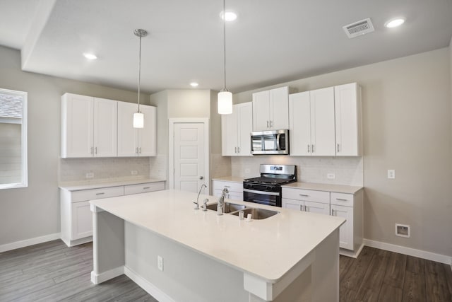 kitchen with appliances with stainless steel finishes, pendant lighting, an island with sink, sink, and white cabinets