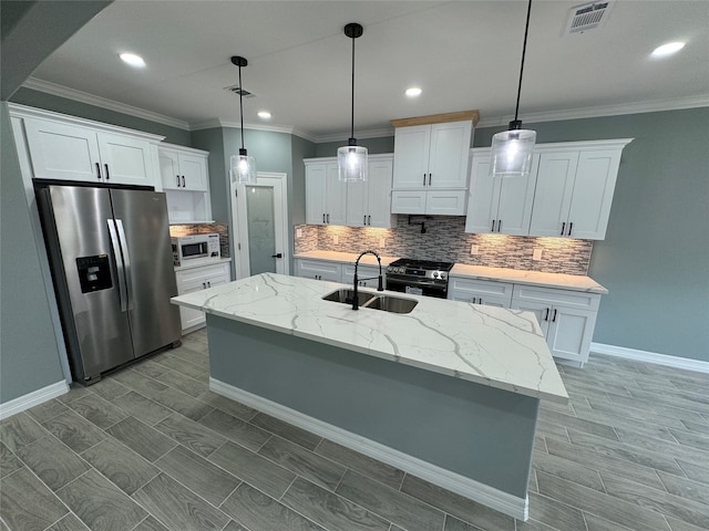 kitchen featuring stainless steel appliances, white cabinetry, light stone countertops, decorative light fixtures, and a kitchen island with sink