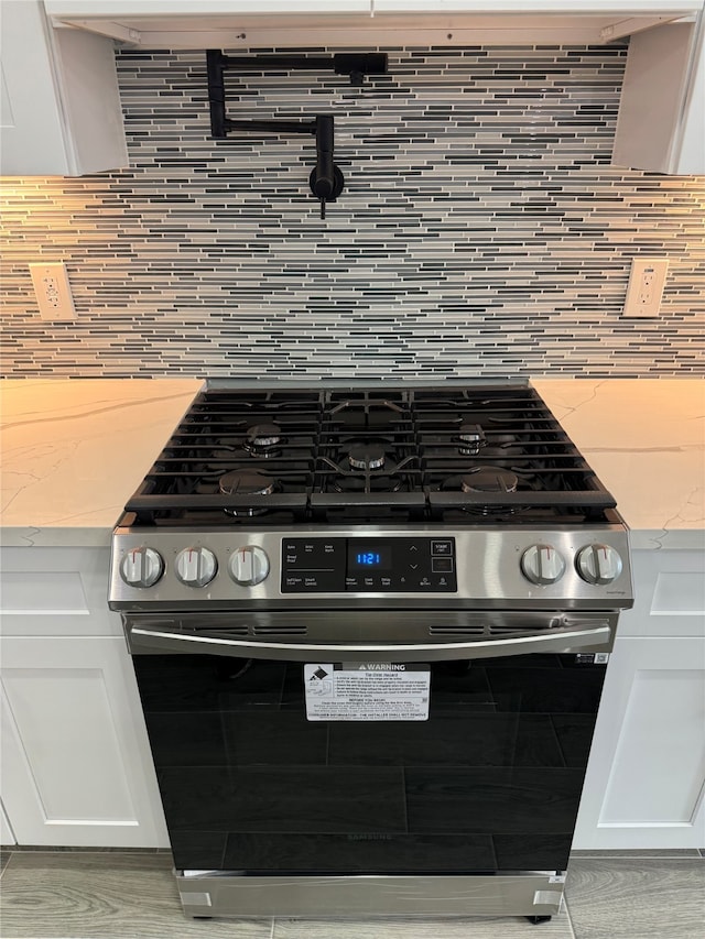 details with white cabinetry, stainless steel gas stove, light stone counters, and backsplash