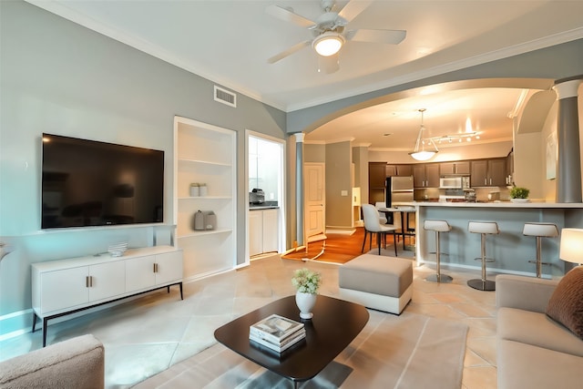 living room featuring light tile patterned floors, crown molding, decorative columns, and ceiling fan