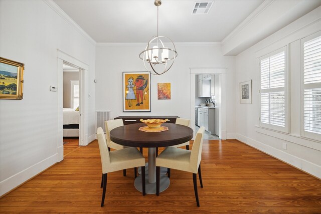 dining room with light hardwood / wood-style floors, crown molding, and an inviting chandelier