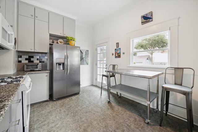 kitchen with ornamental molding, white appliances, backsplash, and dark stone countertops