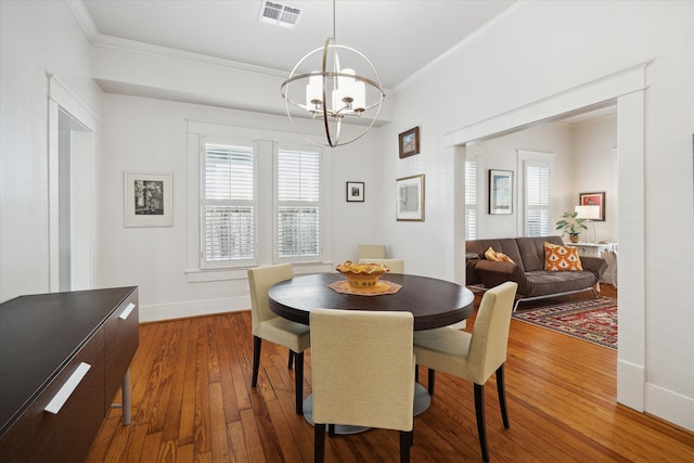 dining space featuring wood-type flooring, crown molding, and a notable chandelier