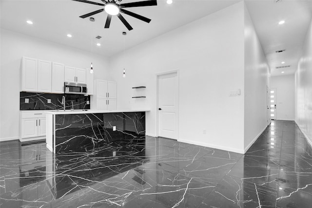 kitchen with sink, ceiling fan, white cabinetry, a towering ceiling, and a kitchen island