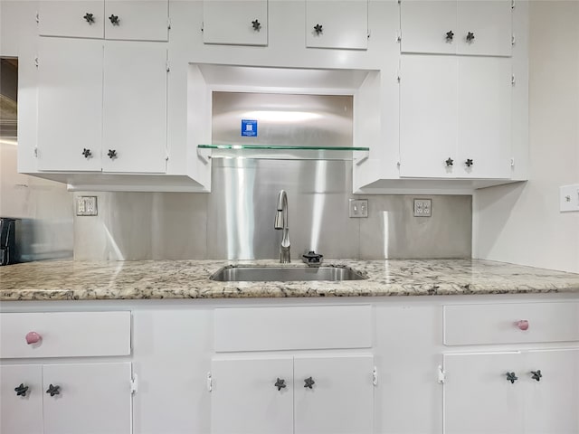 kitchen with white cabinetry, sink, and light stone counters