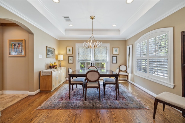 dining space featuring a raised ceiling, hardwood / wood-style floors, a notable chandelier, and ornamental molding