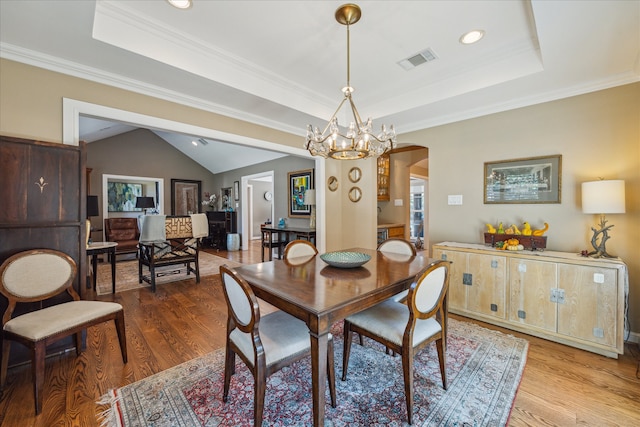 dining room featuring light wood-type flooring, a raised ceiling, vaulted ceiling, crown molding, and a notable chandelier