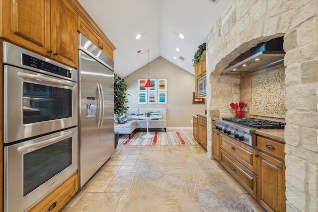 kitchen with pendant lighting, lofted ceiling, wall chimney range hood, built in appliances, and light stone counters