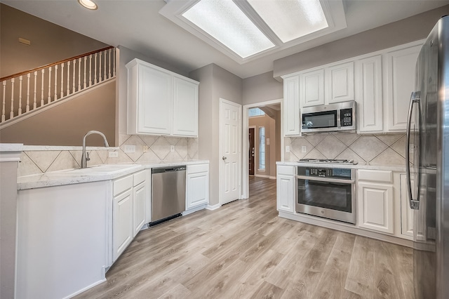 kitchen featuring stainless steel appliances, white cabinets, kitchen peninsula, sink, and light wood-type flooring