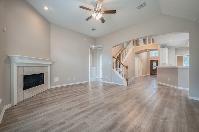 unfurnished living room with light wood-type flooring, a tiled fireplace, lofted ceiling, and ceiling fan