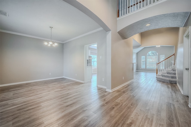 unfurnished room featuring ornamental molding, hardwood / wood-style floors, a towering ceiling, and an inviting chandelier