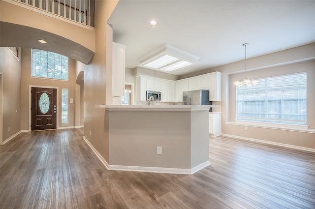 kitchen featuring a towering ceiling, appliances with stainless steel finishes, light hardwood / wood-style floors, white cabinets, and kitchen peninsula