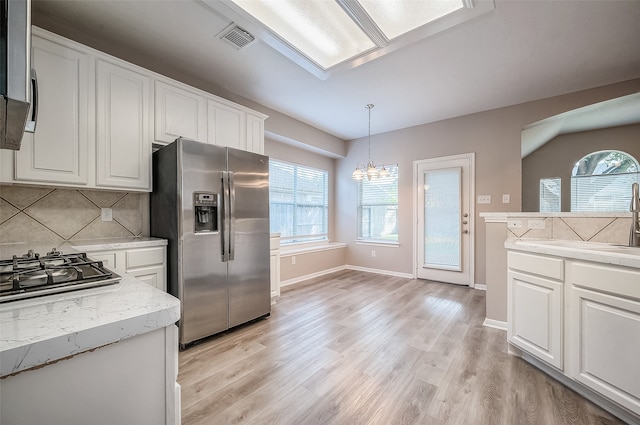 kitchen with stainless steel appliances, white cabinetry, hanging light fixtures, decorative backsplash, and light hardwood / wood-style floors