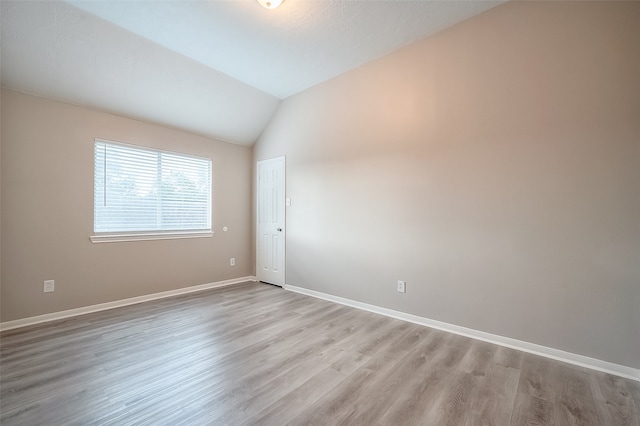 spare room with light hardwood / wood-style floors and lofted ceiling