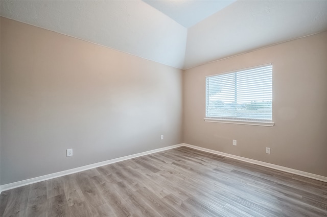 spare room with light wood-type flooring and lofted ceiling