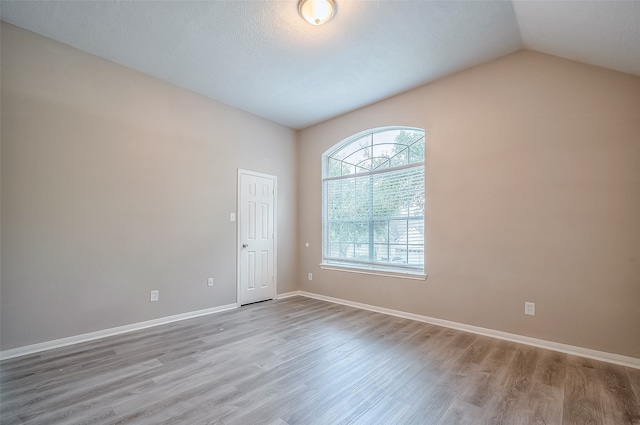 spare room with lofted ceiling, a textured ceiling, and light hardwood / wood-style flooring