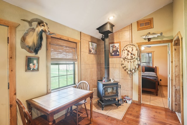 dining room featuring hardwood / wood-style floors, a wealth of natural light, a wood stove, and vaulted ceiling