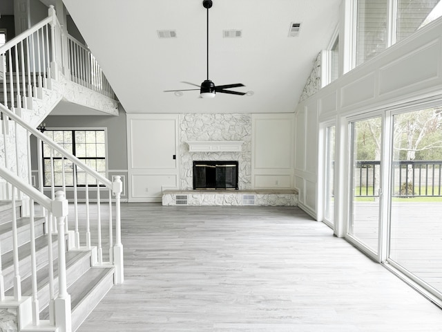 unfurnished living room with high vaulted ceiling, a stone fireplace, hardwood / wood-style floors, and a healthy amount of sunlight